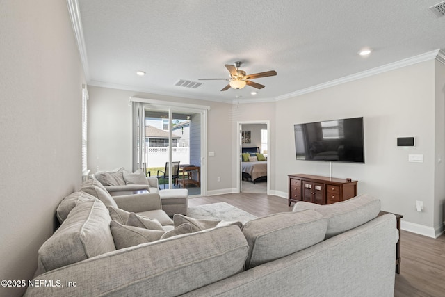 living room featuring visible vents, ornamental molding, baseboards, and wood finished floors