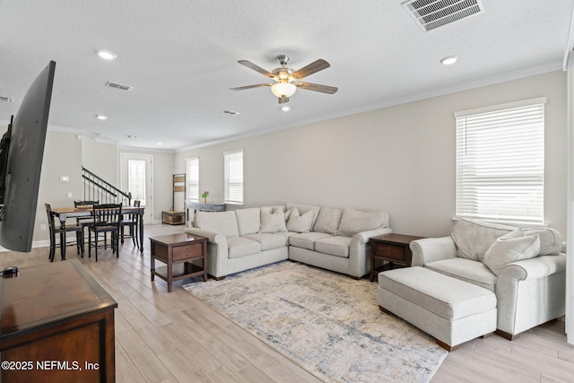 living area with visible vents, light wood-style floors, and ornamental molding