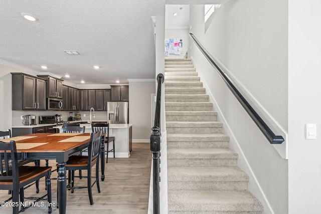 staircase with wood finished floors, baseboards, recessed lighting, ornamental molding, and a textured ceiling