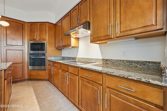 kitchen featuring under cabinet range hood, light stone counters, stainless steel appliances, light tile patterned flooring, and brown cabinetry