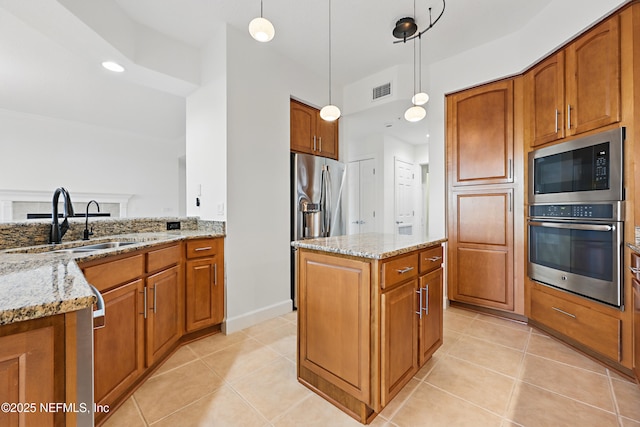 kitchen with a sink, light stone counters, appliances with stainless steel finishes, brown cabinetry, and light tile patterned floors