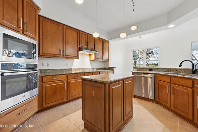 kitchen with under cabinet range hood, dark stone counters, light tile patterned flooring, stainless steel appliances, and a sink