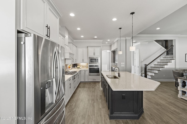 kitchen with wood finished floors, ornamental molding, a sink, white cabinets, and appliances with stainless steel finishes