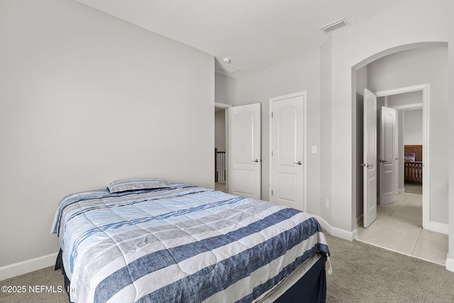 bedroom featuring visible vents, light carpet, arched walkways, and baseboards