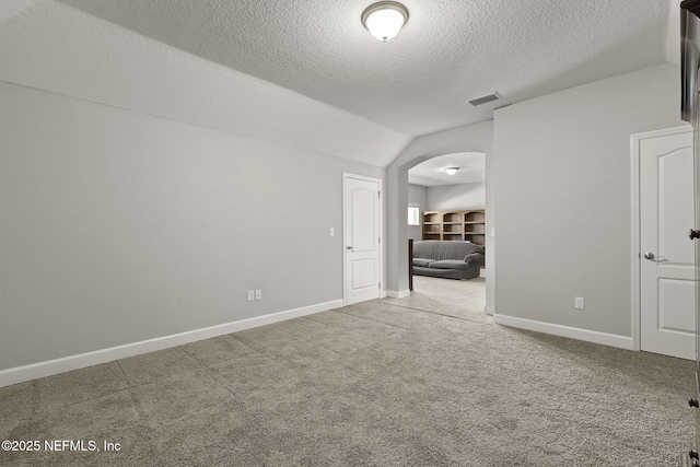 carpeted empty room with visible vents, baseboards, arched walkways, vaulted ceiling, and a textured ceiling