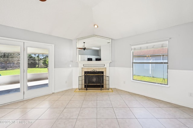 unfurnished living room with a wainscoted wall, a fireplace, ceiling fan, vaulted ceiling, and tile patterned floors