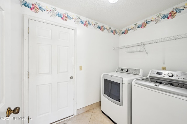 laundry area featuring a textured ceiling, separate washer and dryer, light tile patterned flooring, baseboards, and laundry area