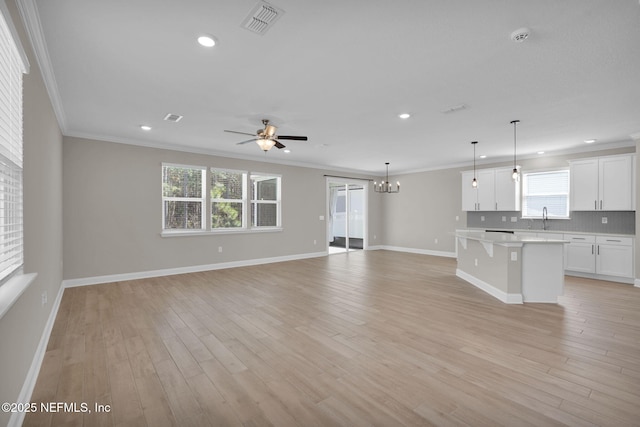 unfurnished living room with visible vents, light wood-style flooring, ornamental molding, a sink, and baseboards