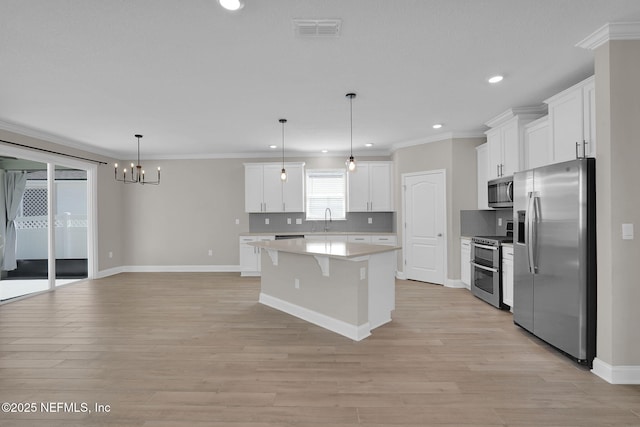 kitchen featuring visible vents, a kitchen island, white cabinets, stainless steel appliances, and a sink