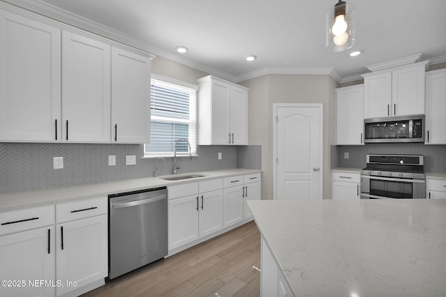 kitchen featuring light wood finished floors, ornamental molding, stainless steel appliances, white cabinetry, and a sink