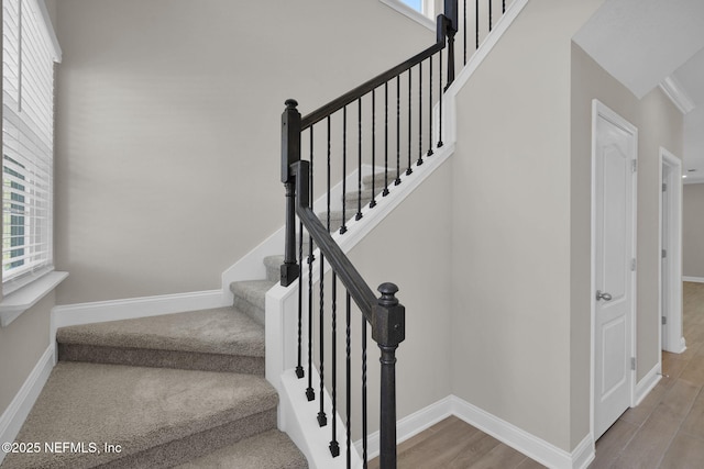 stairway with a high ceiling, baseboards, and wood finished floors