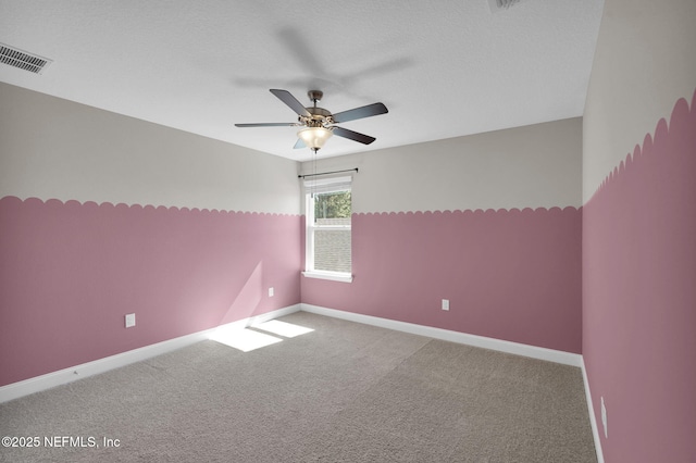 carpeted spare room featuring baseboards, visible vents, and ceiling fan