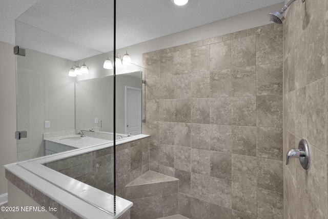 bathroom featuring a textured ceiling, tiled shower, and vanity