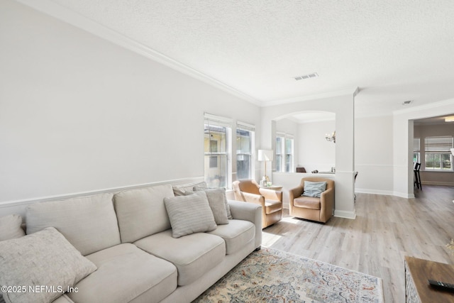 living area with light wood finished floors, visible vents, ornamental molding, arched walkways, and a textured ceiling