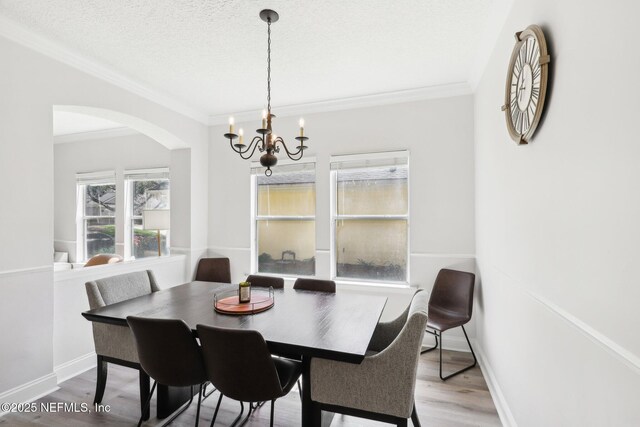 dining space with crown molding, an inviting chandelier, wood finished floors, arched walkways, and a textured ceiling