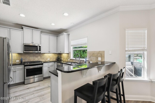 kitchen featuring dark countertops, visible vents, appliances with stainless steel finishes, a peninsula, and a sink