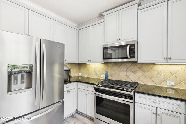 kitchen featuring light wood-type flooring, stainless steel appliances, dark stone counters, white cabinets, and decorative backsplash