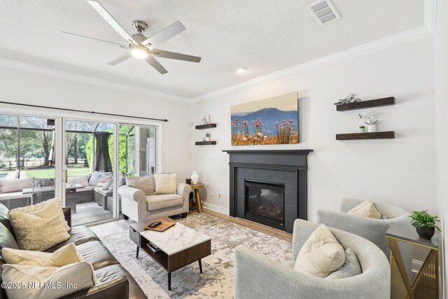 living room with a ceiling fan, wood finished floors, visible vents, a tile fireplace, and ornamental molding