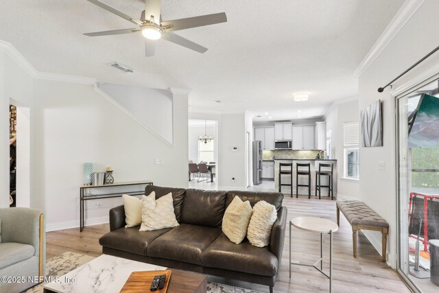 living room with visible vents, light wood-style flooring, ceiling fan with notable chandelier, crown molding, and a healthy amount of sunlight