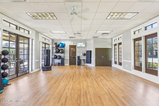 workout room with a drop ceiling, a healthy amount of sunlight, french doors, and wood finished floors