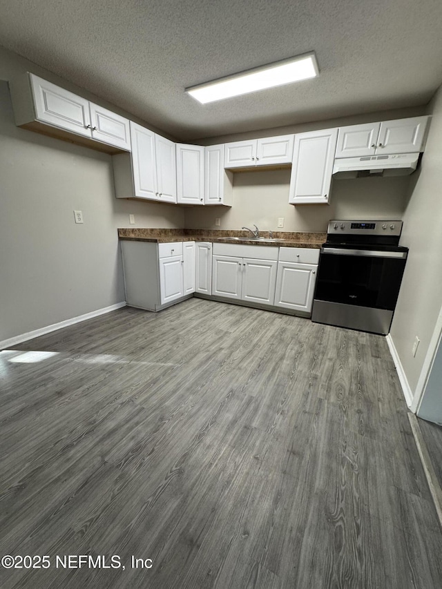 kitchen with under cabinet range hood, stainless steel electric range oven, dark countertops, and white cabinets