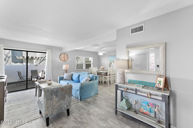 living room featuring visible vents, a textured ceiling, a ceiling fan, and wood finished floors