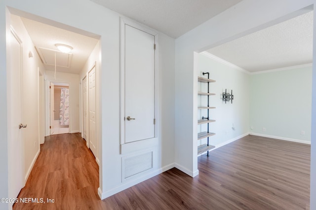 corridor with visible vents, a textured ceiling, attic access, and wood finished floors