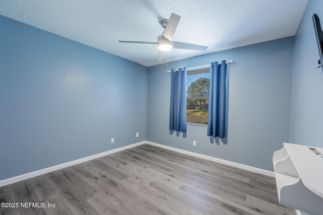 unfurnished room with ceiling fan, a textured ceiling, baseboards, and wood finished floors