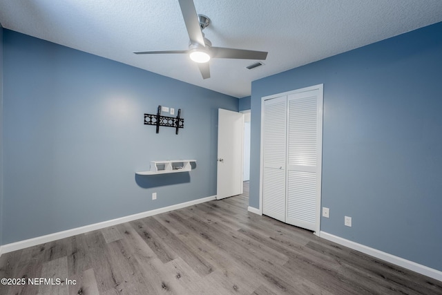 unfurnished bedroom featuring visible vents, a textured ceiling, wood finished floors, a closet, and baseboards