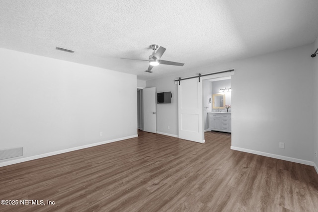 unfurnished bedroom featuring a barn door, baseboards, visible vents, and wood finished floors