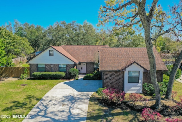 view of front of property with brick siding, concrete driveway, a front lawn, and fence