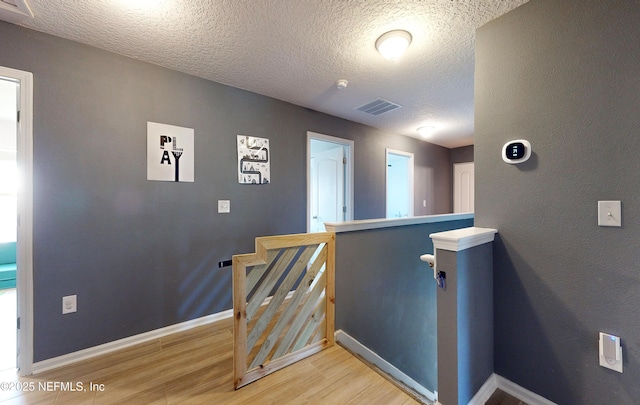 stairs with a textured ceiling, wood finished floors, visible vents, and baseboards