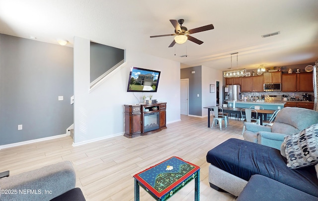 living room with stairway, a ceiling fan, baseboards, visible vents, and light wood-type flooring