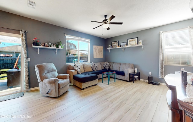 living room with visible vents, baseboards, light wood-style flooring, and a ceiling fan