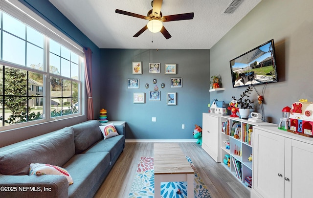 living area with visible vents, ceiling fan, baseboards, wood finished floors, and a textured ceiling