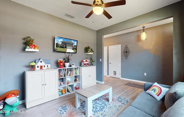 living area with visible vents, light wood-style flooring, a textured ceiling, baseboards, and ceiling fan