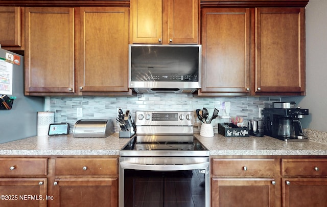 kitchen with decorative backsplash, brown cabinets, appliances with stainless steel finishes, and light countertops