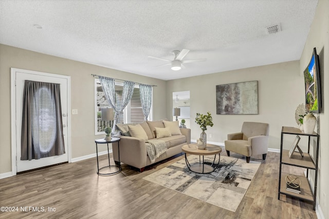 living area with visible vents, a textured ceiling, baseboards, and wood finished floors