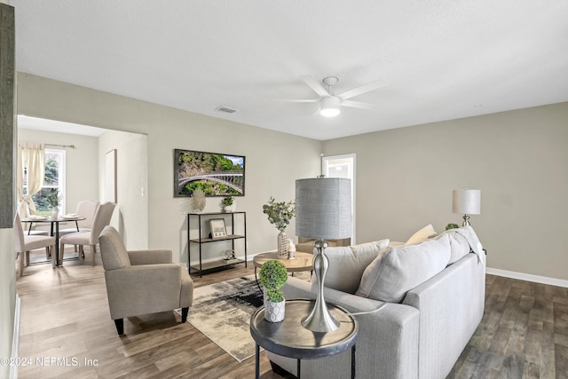 living room featuring dark wood-type flooring, visible vents, baseboards, and ceiling fan