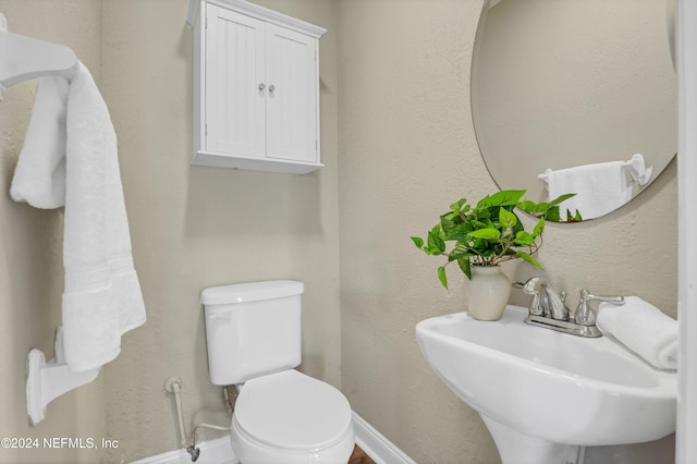 bathroom featuring a textured wall, toilet, baseboards, and a sink