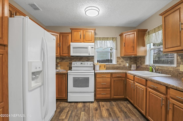 kitchen with visible vents, a sink, brown cabinets, white appliances, and dark wood-style flooring