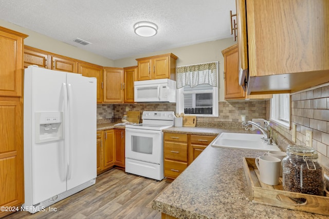 kitchen with visible vents, light wood-type flooring, a sink, white appliances, and decorative backsplash