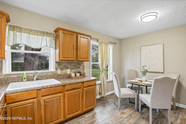 kitchen featuring baseboards, decorative backsplash, wood finished floors, brown cabinetry, and a sink