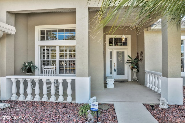 view of exterior entry with stucco siding and a porch