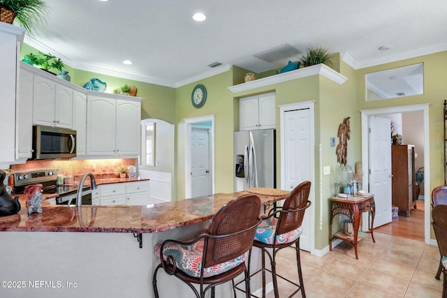 kitchen with a breakfast bar area, dark stone counters, ornamental molding, a peninsula, and stainless steel appliances