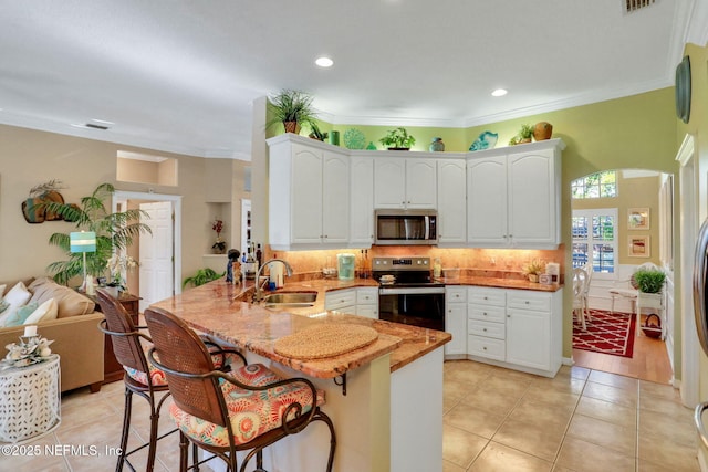 kitchen with appliances with stainless steel finishes, white cabinetry, a peninsula, and a sink