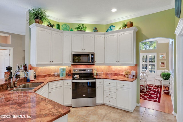 kitchen featuring light tile patterned floors, arched walkways, a sink, appliances with stainless steel finishes, and crown molding