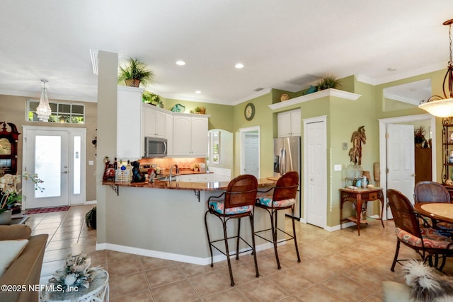 kitchen with a breakfast bar area, a peninsula, light tile patterned flooring, appliances with stainless steel finishes, and crown molding