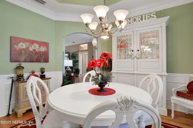 dining room with wood finished floors, a wainscoted wall, arched walkways, ornamental molding, and a notable chandelier