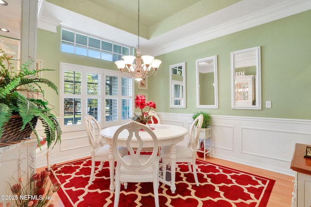 dining space featuring a wainscoted wall, ornamental molding, wood finished floors, an inviting chandelier, and a raised ceiling